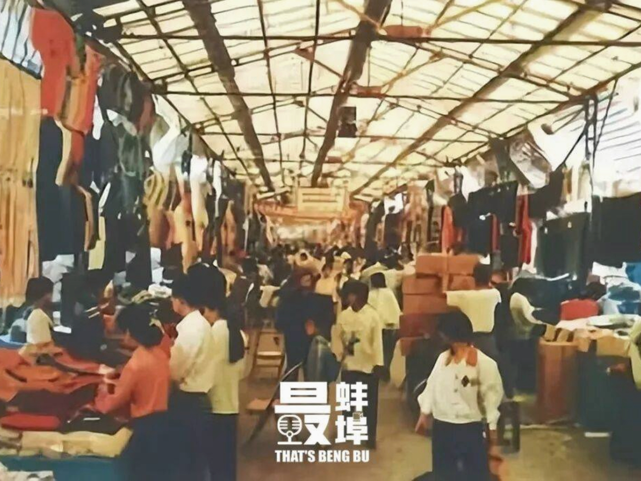 相似环境参考,非原始现场照片:市场通道两侧分布着摊位,上方可见顶棚结构;保留所提供材料上的原有文字。